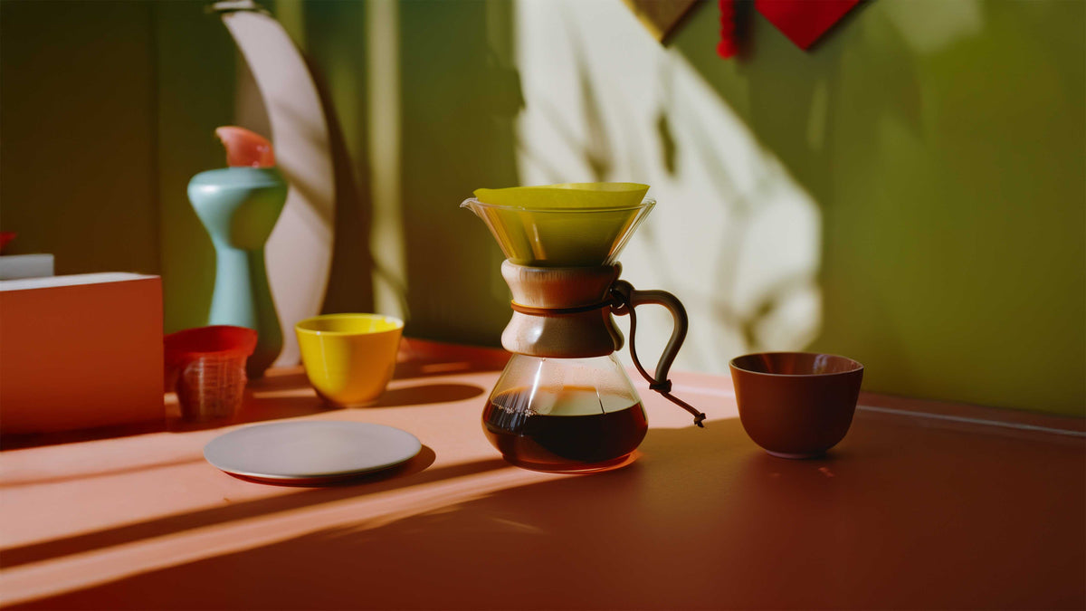 A pour-over dripper and glass coffee server on a sunlit table